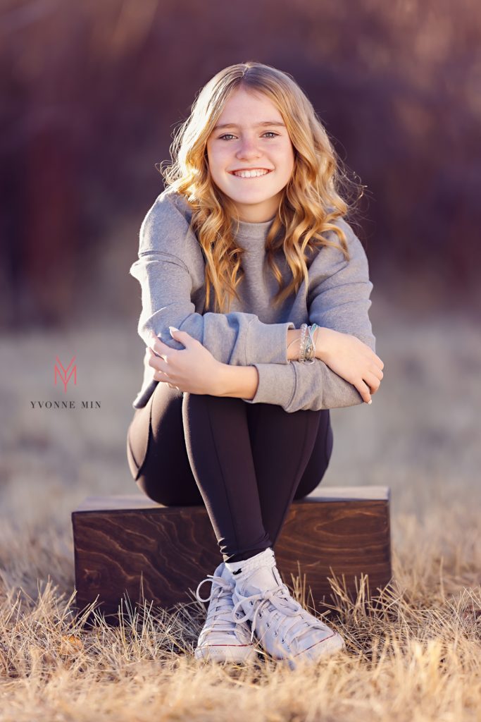 A teen girl poses on a box during her family photoshoot with Yvonne Min in Thornton, Colorado.