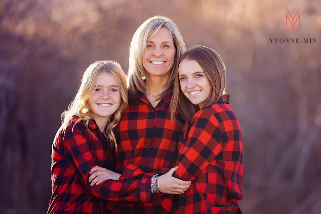 A mom and her two teenage daughters pose in matching red pajamas at their family photoshoot.