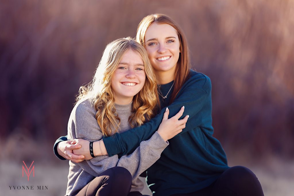 Two sisters hug each other during their family photoshoot outside with Yvonne Min Photography.