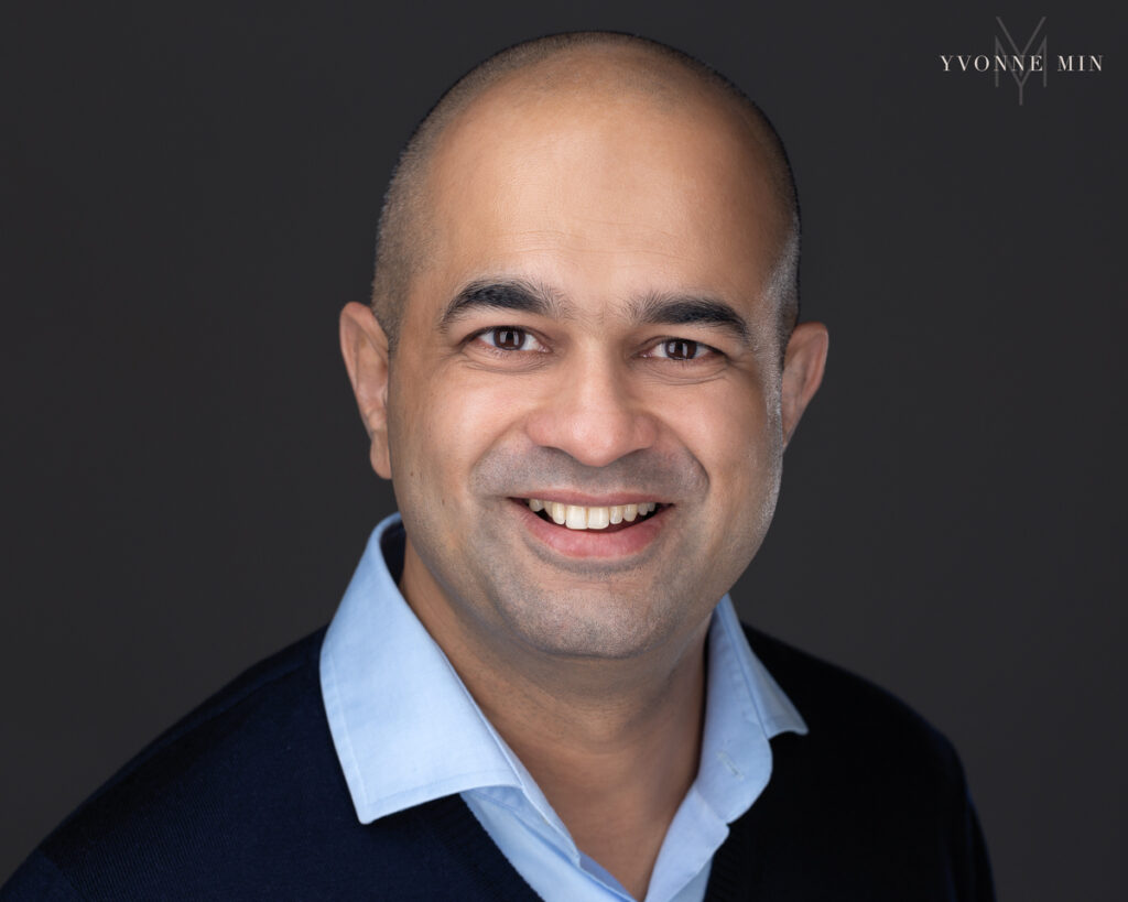 Business man dressed in a black sweater and blue shirt headshot by Yvonne Min.