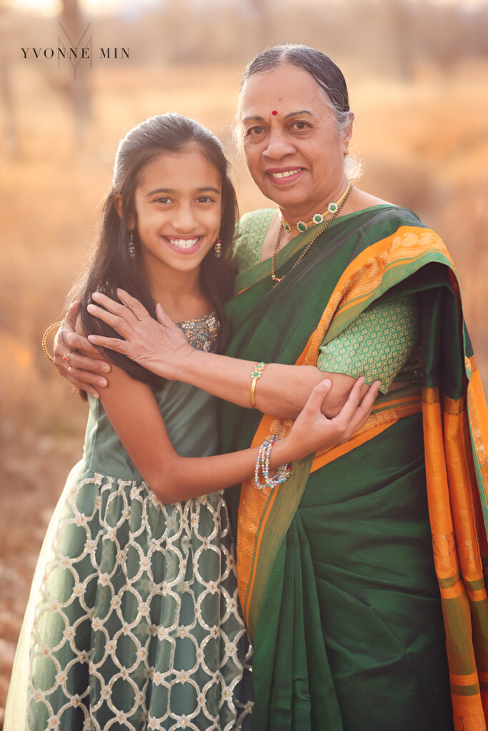 Grandmother and granddaughter hug in green sarees at their family photoshoot.