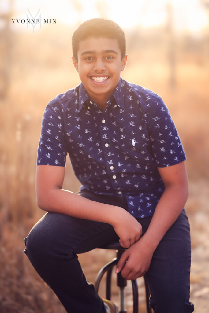 Teenage boy sits on a stool in the sunset at a family photoshoot with Yvonne Min Photography..