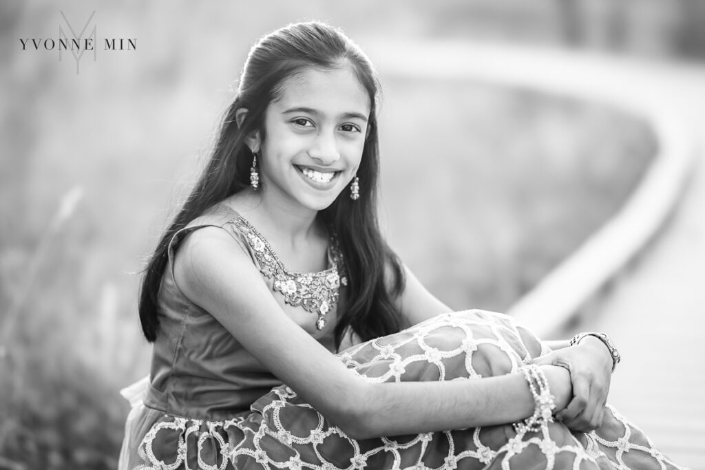 A young Indian girl sits on a bridge in a traditional green saree during a family photoshoot.