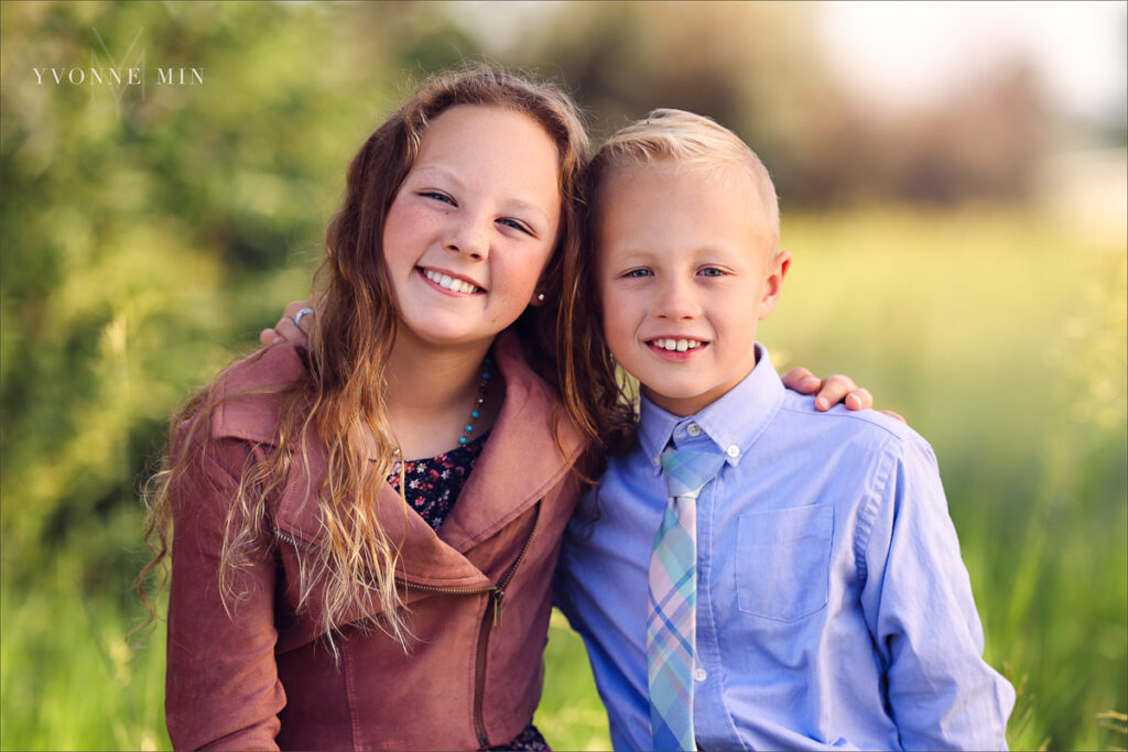 A photograph of a brother and sister sitting on a fence during their family photoshoot at McKay Lake in Westminster, Colorado with Yvonne Min Photography.