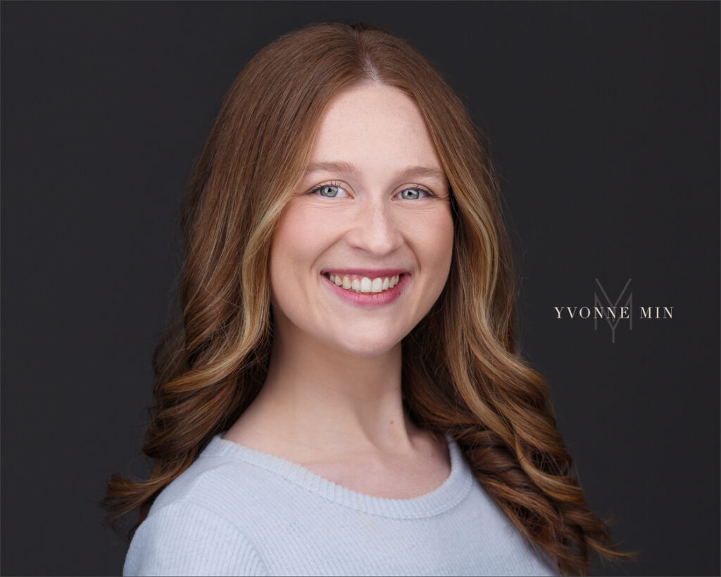 A headshot of a young behavioral therapist on a dark gray background photographed by Yvonne Min Photography in Thornton, Colorado.