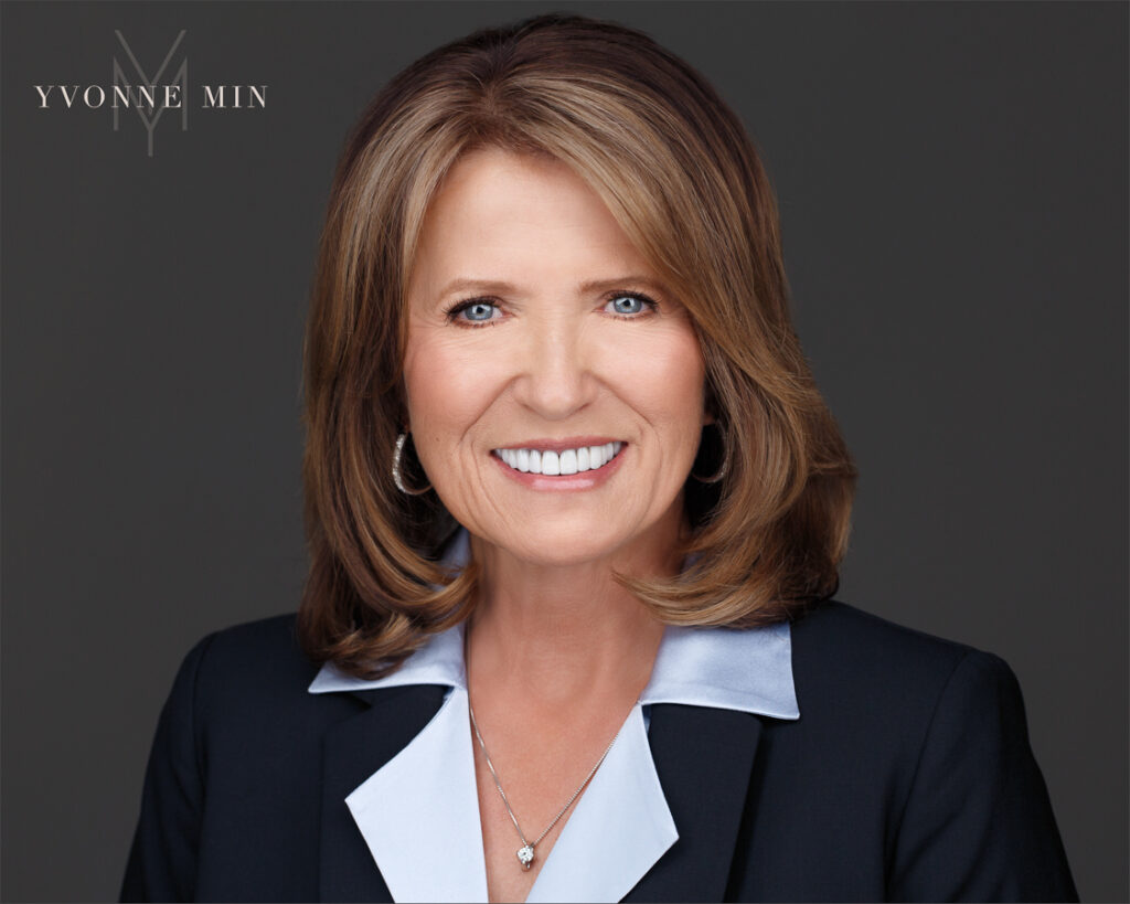 A headshot of a woman in a leadership position at the Conference Board photographed in a blue suit on a dark gray backdrop by Yvonne Min Photography in Thornton, Colorado.