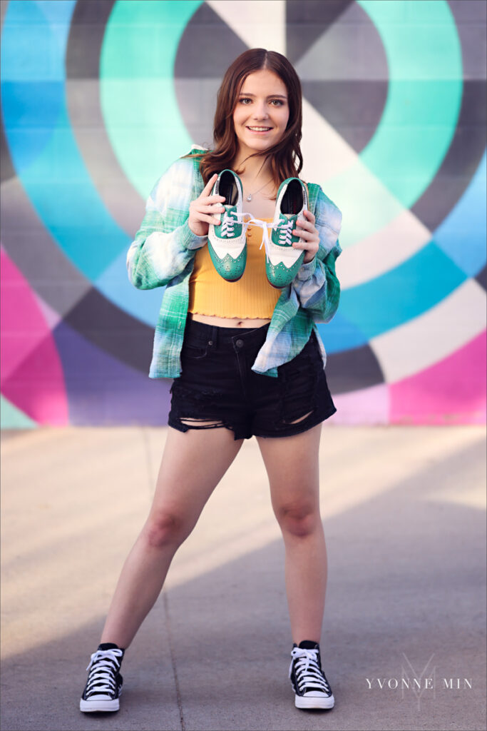 A high school senior poses in front of a colorful mural in the RiNo Art District of Denver with Yvonne Min Photography.