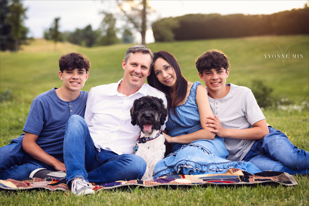 A family sits on a colorful blanket with their dog at their family photography session with Yvonne Min Photography in Purple Park, Colorado.