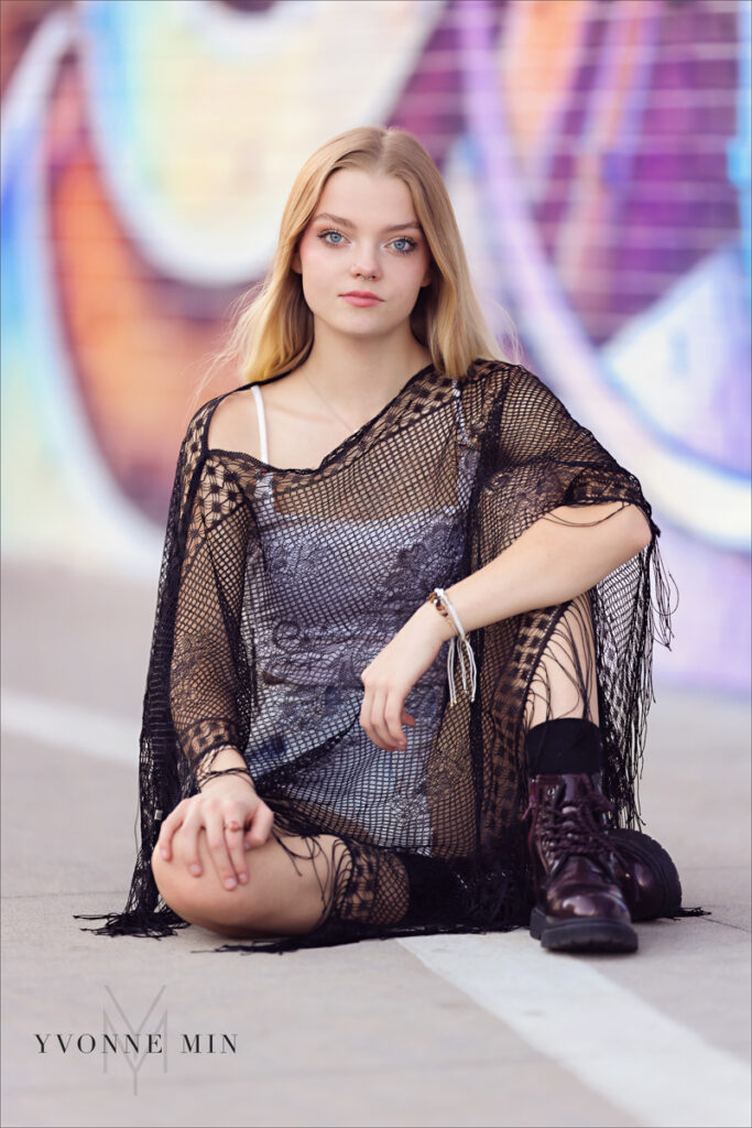 A high school senior poses on the ground in front of a colorful mural in the RiNo Art District of Denver with Yvonne Min Photography.