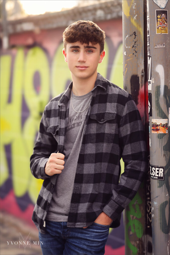 A high school senior boy poses in front of a colorful mural in the RiNo Art District of Denver with Yvonne Min Photography.