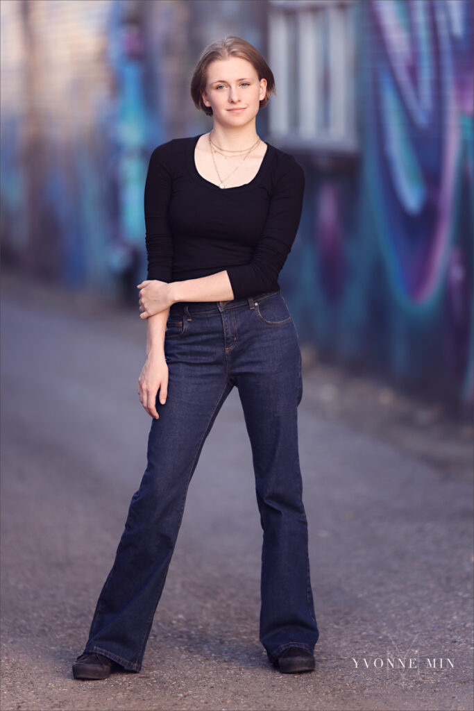 A high school senior girl poses in front of a colorful mural in the RiNo Art District of Denver with Yvonne Min Photography.