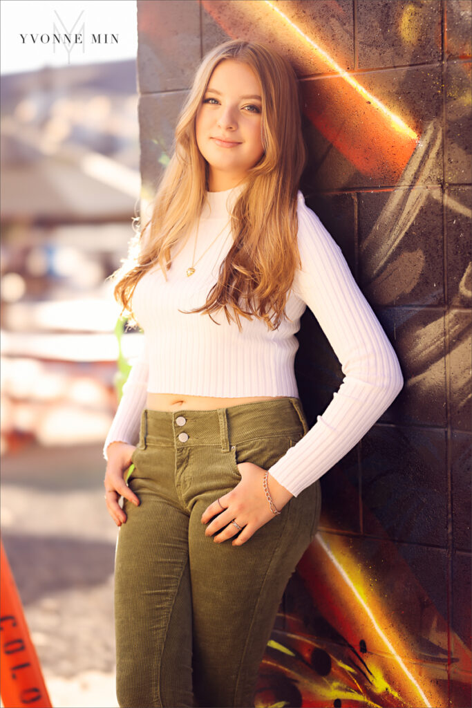 A high school senior girl poses in front of a colorful mural in the RiNo Art District of Denver with Yvonne Min Photography.