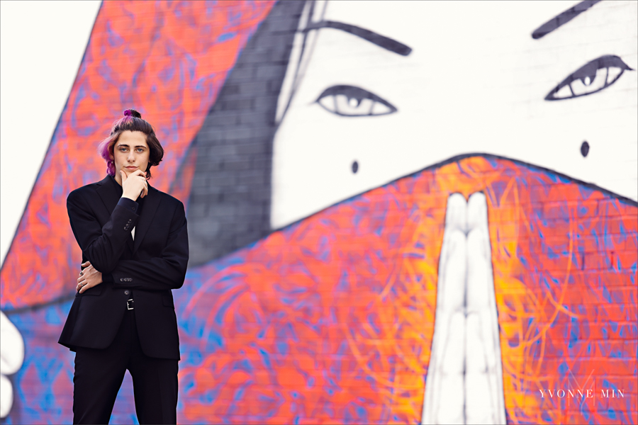 A high school senior boy poses in front of a colorful mural in the RiNo Art District of Denver, Colorado with Yvonne Min Photography.