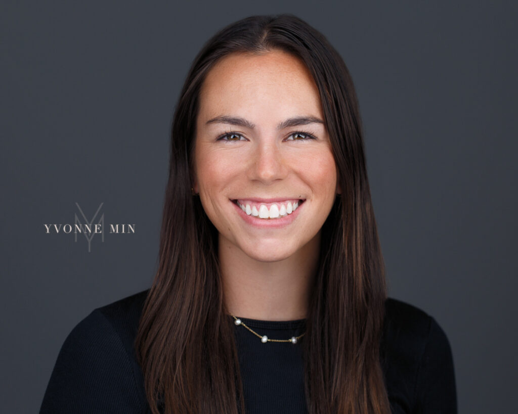 A headshot of a young behavioral therapist on a dark gray background taken in the studio of Yvonne Min Photography in Thornton, Colorado.