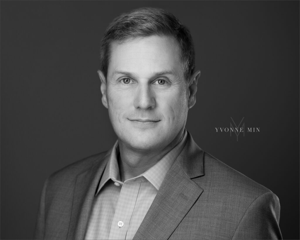 A black and white headshot of an aviation professional taken on a dark gray backdrop by Yvonne Min Photography in Thornton, Colorado.