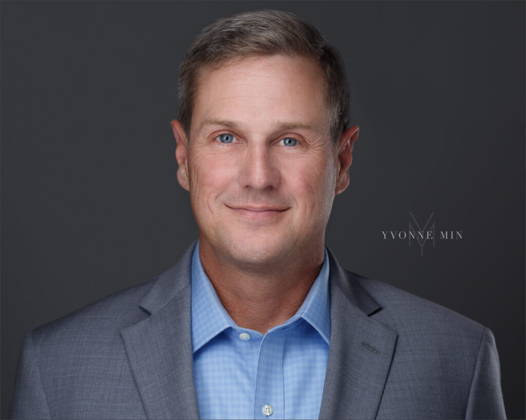 A black and white headshot of an aviation professional taken on a dark gray backdrop by Yvonne Min Photography in Thornton, Colorado.