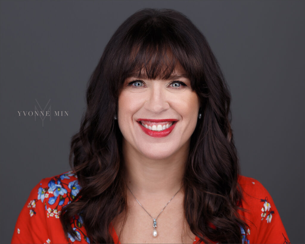 A new headshot of a Boulder therapist wearing a red shirt on a dark gray background taken by Yvonne Min Photography in Thornton, Colorado.