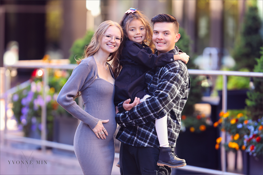 A photograph of an expecting mom and her husband holding their young daughter taken outside Union Station in downtown Denver by Yvonne Min Photography.