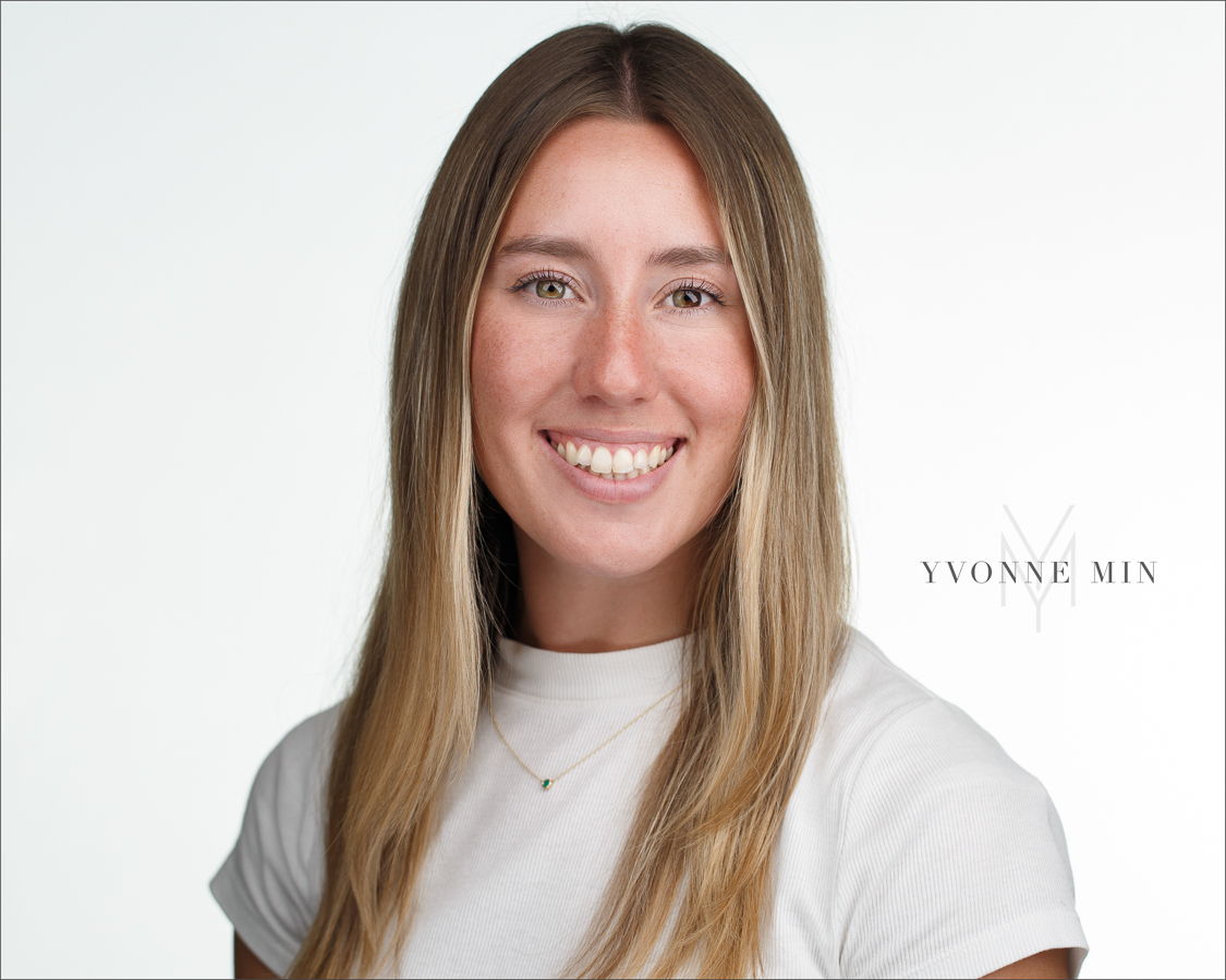 A headshot of a young woman in a white shirt on a white backdrop photographed by Yvonne Min Photography in Thornton, Colorado.