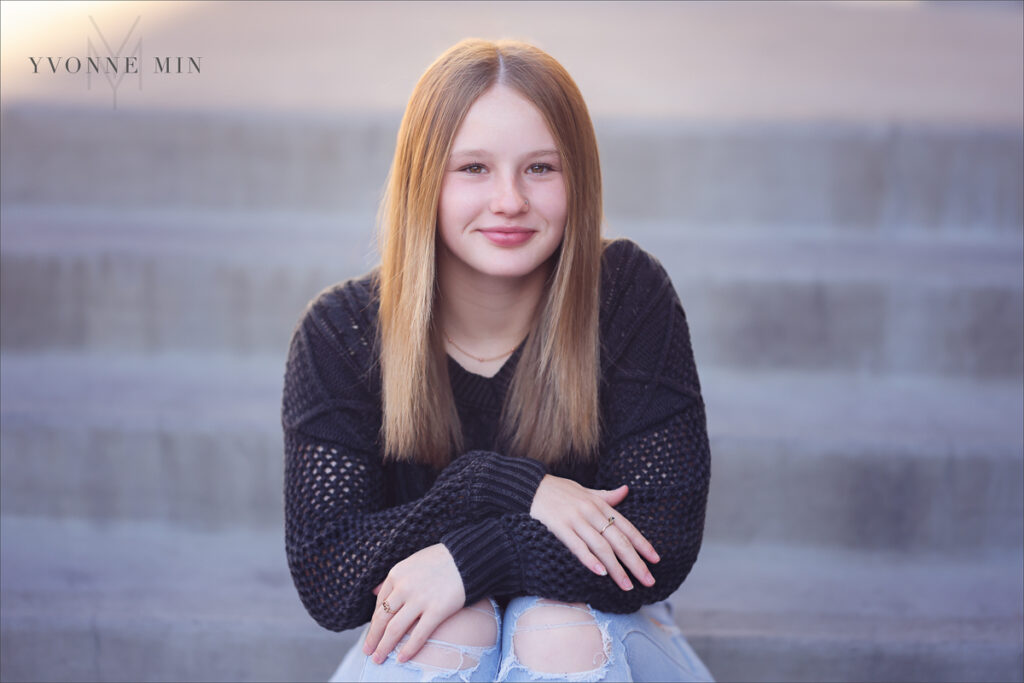 A teen girl sits on the concrete steps outside Union Station in LoDo Denver during a family photography session with Yvonne Min Photography.