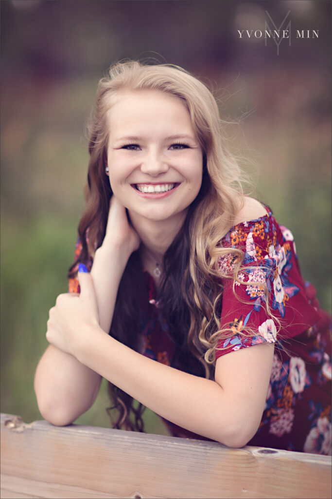 A senior picture of a high school student leaning on a fence taken at McKay Lake by Yvonne Min Photography.