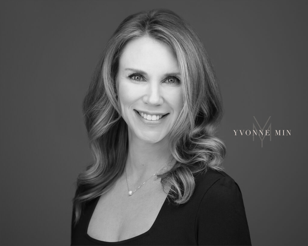 A professional new black and white headshot for a business woman wearing a black shirt on a gray backdrop at the studio of Yvonne Min Photography in Thornton, Colorado.