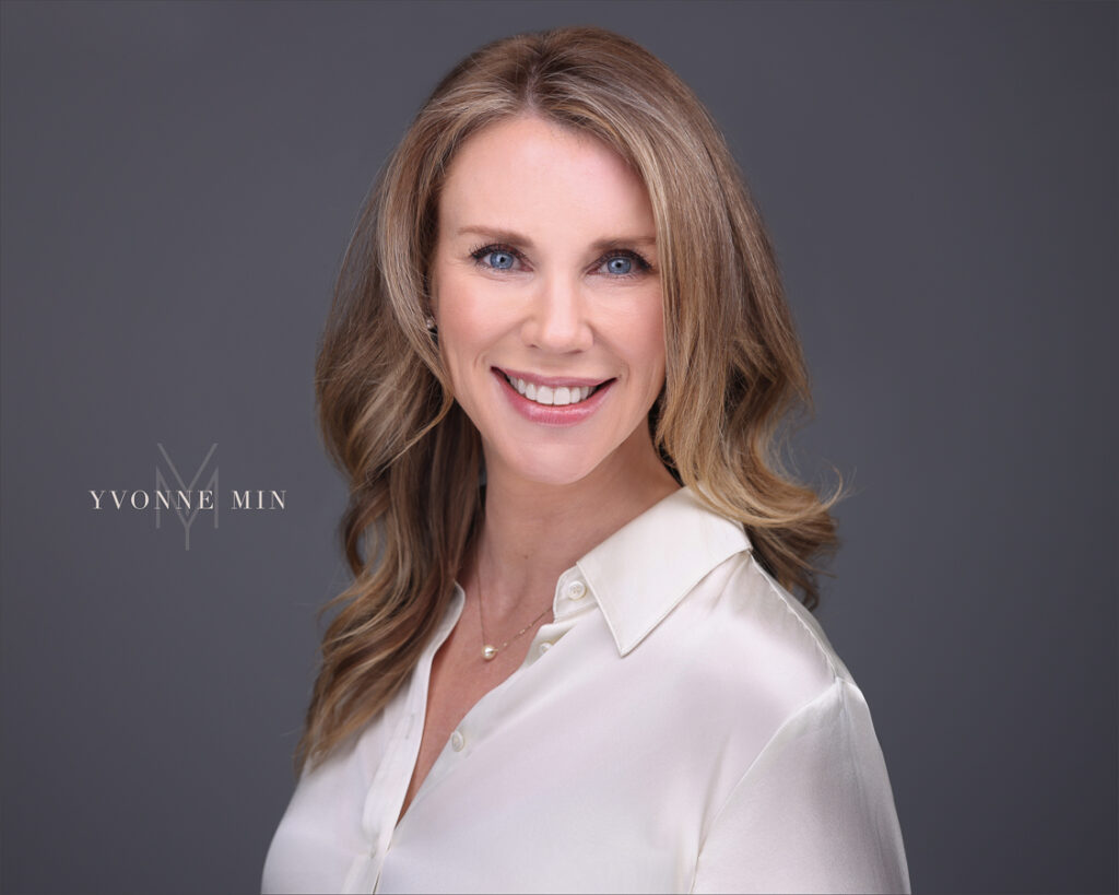 A professional new headshot for a business woman in a white shirt on a gray backdrop at the studio of Yvonne Min Photography in Thornton, Colorado.