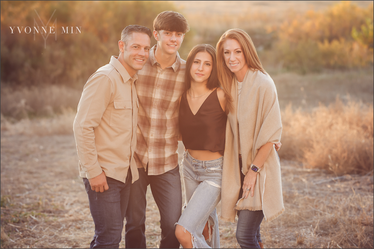 A family of four poses together with the sunset behind them in Thornton, Colorado during their family photoshoot with Yvonne Min Photography.