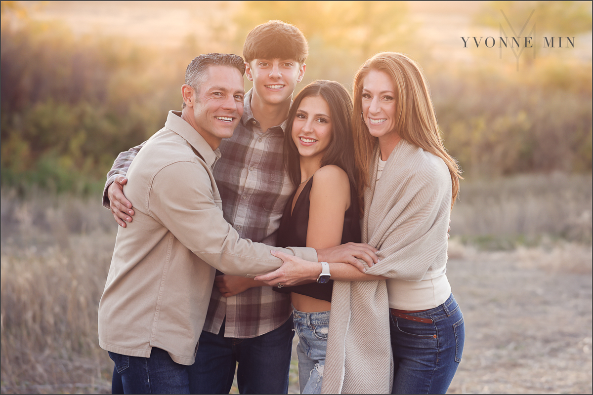 A family of four poses together with the sunset behind them in Thornton, Colorado during their family photoshoot with Yvonne Min Photography.