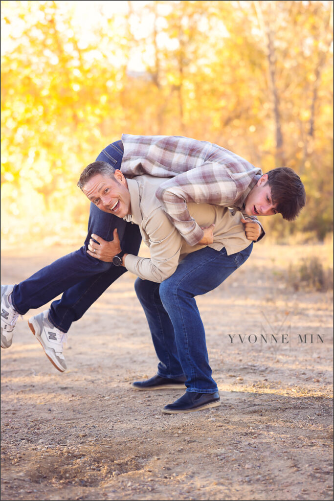 A dad lifts up his teenage son at their family photoshoot in Thornton, Colorado with Yvonne Min Photography.