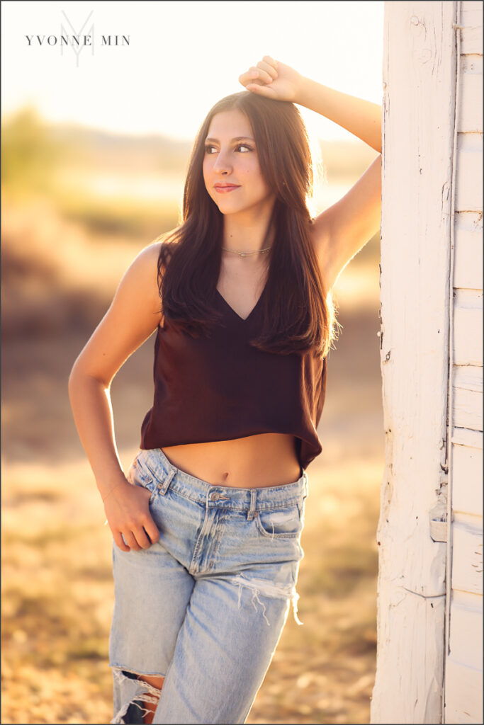 A young teen girl leans against a white barn wall during her family photography session with Yvonne Min Photography in Thornton, Colorado.