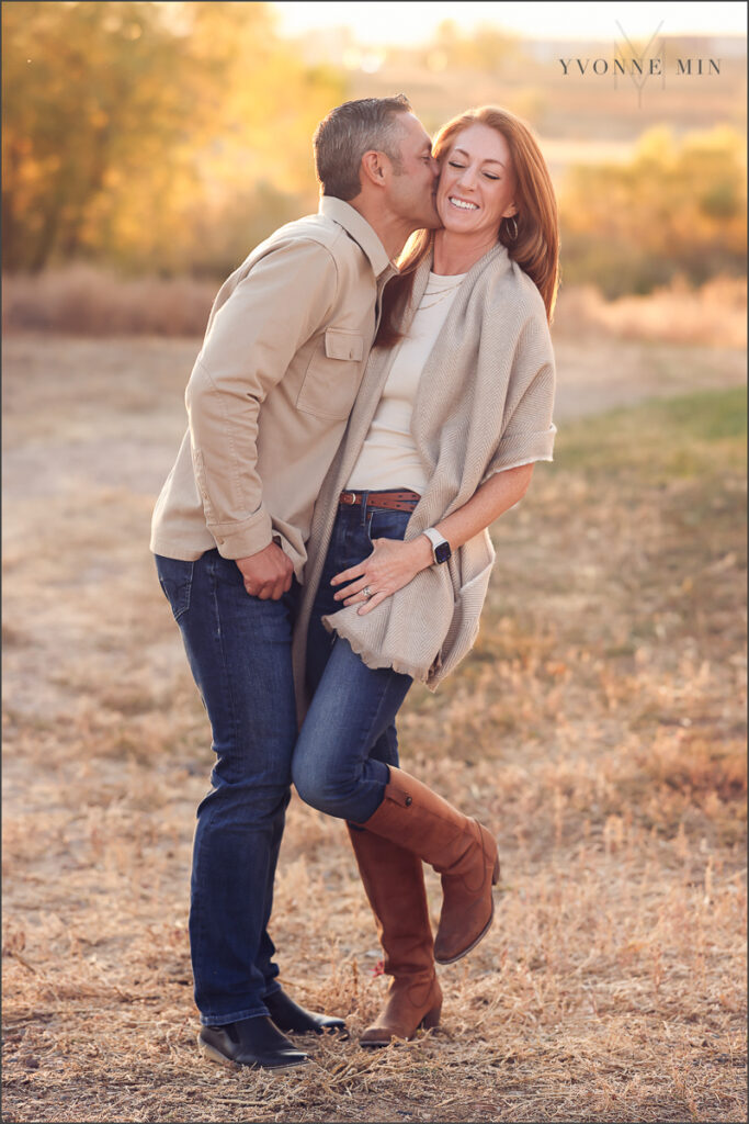 A dad kisses a mom on the check while she laughs during their family photography session in Thornton, Colorado with Yvonne Min Photography.