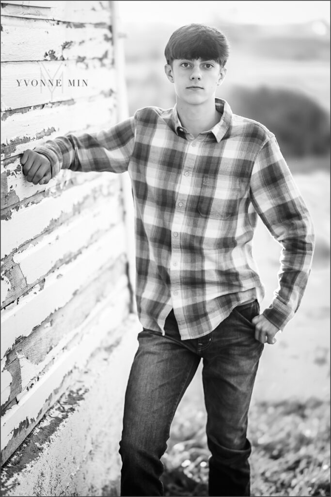 A teen girl leans against a white barn wall during his family photography session with Yvonne Min Photography in Thornton, Colorado.