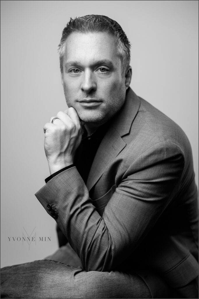 A photograph of  a man running for Thornton City Council photographed by Yvonne Min Photography on a gray backdrop at her studio in Thornton, Colorado.