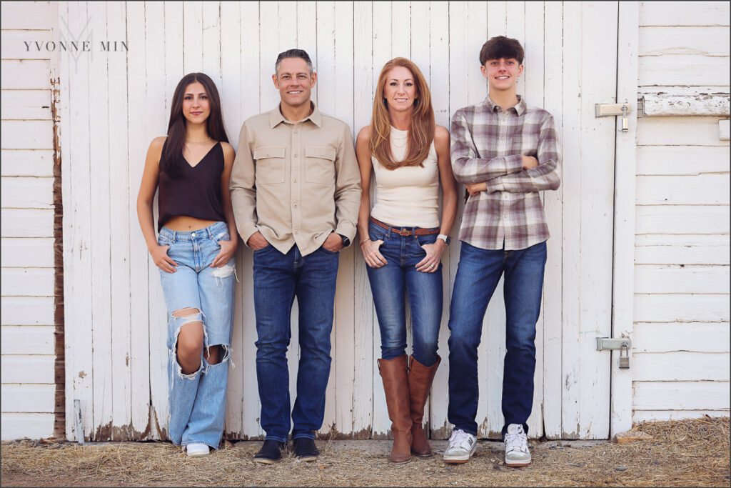 A family of four leans against a white barn during their photography session with Yvonne Min Photography in Thornton, Colorado.