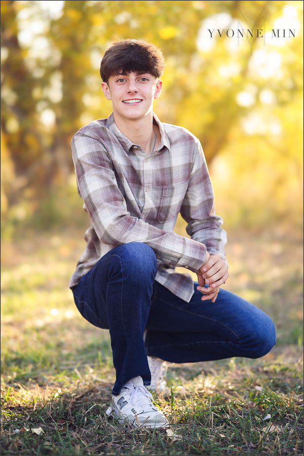 A teen boy squats for a photo at his family photography session with Yvonne Min Photography in Thornton, Colorado.