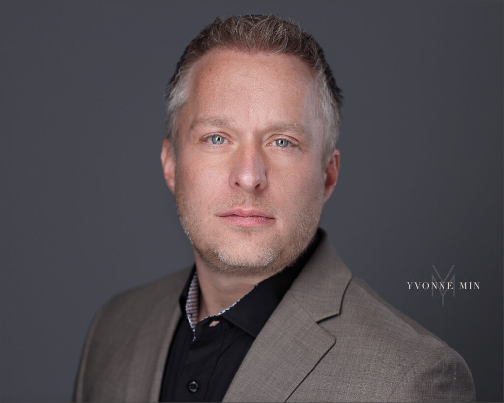 A new headshot for a man running for Thornton City Council photographed by Yvonne Min Photography on a dark gray backdrop at her studio in Thornton, Colorado.