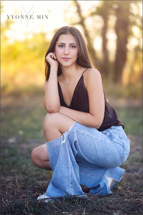 A teen girl squats for a photo at her family photography session with Yvonne Min Photography in Thornton, Colorado.