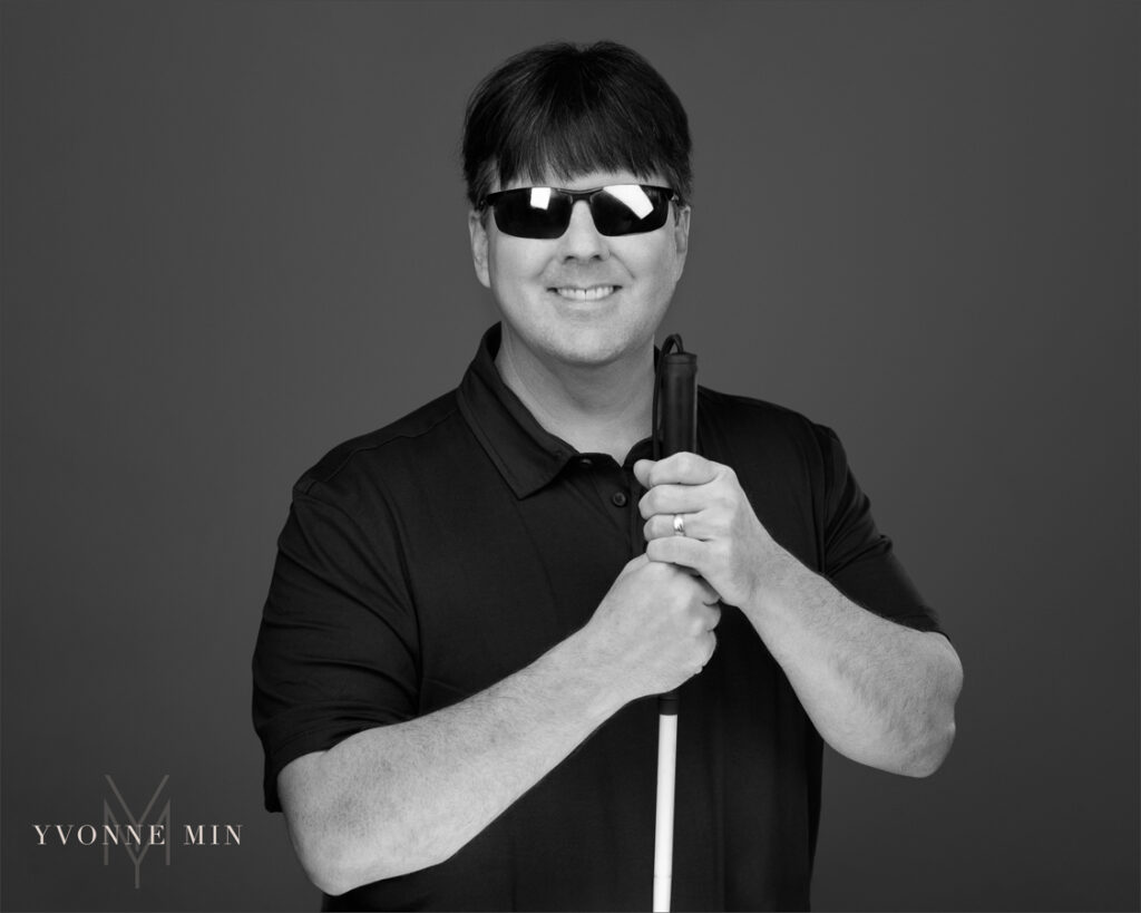 A black and white headshot of the founder of the Blind Institute of Technology taken at the Yvonne Min Photography Studio in Thornton, Colorado on a dark gray backdrop.