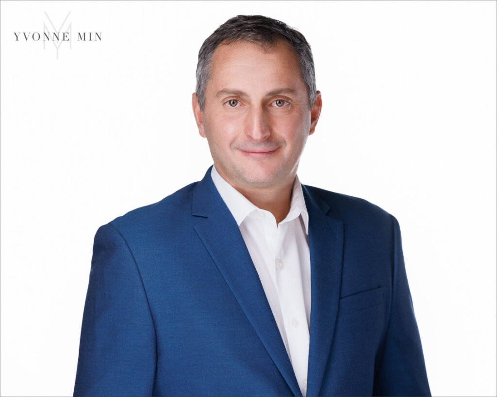 A new corporate headshot of a professional man in a blue jacket on a white backdrop photographed in the studio of Yvonne Min Photography in Thornton, Colorado.