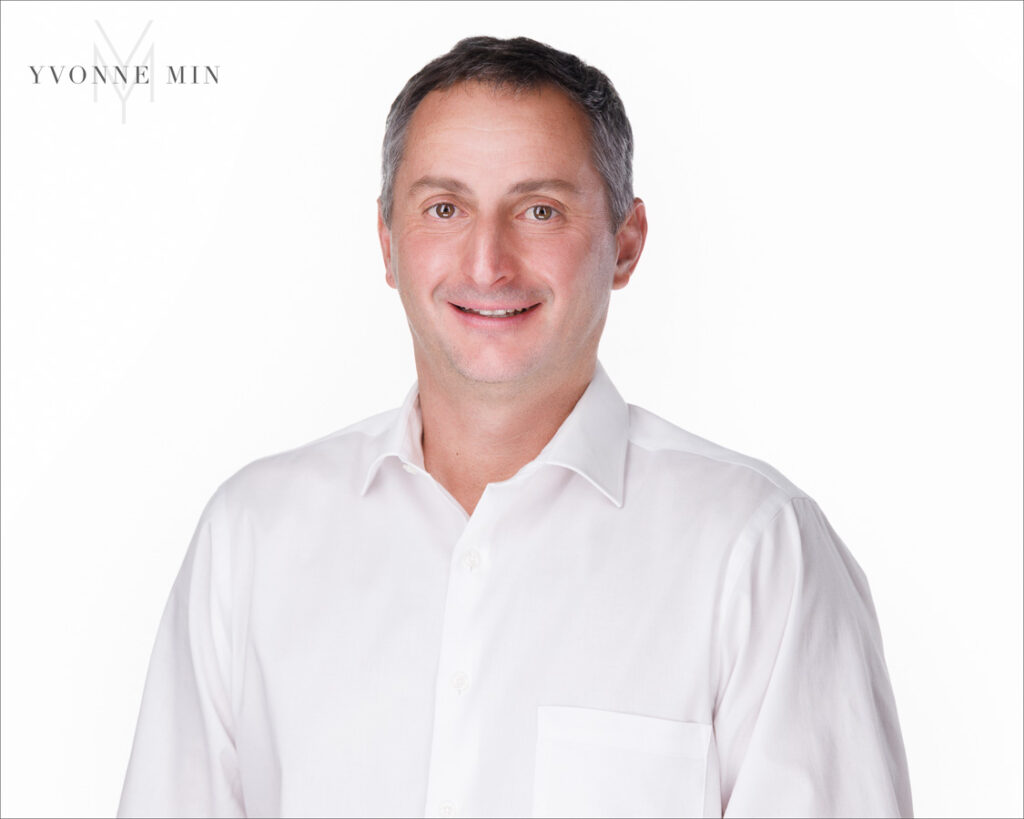 A new headshot of a business professional in a white dress shirt on a white backdrop photographed in the studio of Yvonne Min Photography in Thornton, Colorado.
